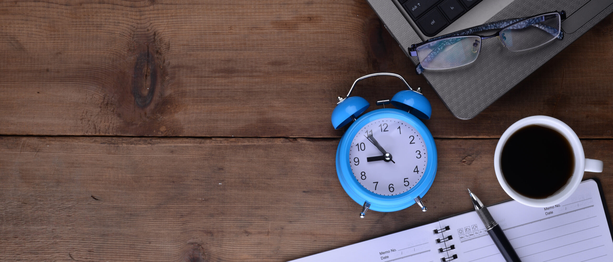 Desk with notebook, clock, laptop, and coffee representing time off policy planning and PTO tracking