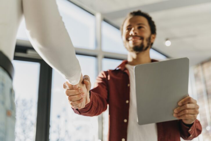 Manager shaking hands with departing employee while holding tablet during employee offboarding checklist process